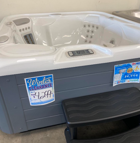 A white hot tub with a grey exterior, black steps, and two winter clearance signs priced at $4,299 and $4,799.