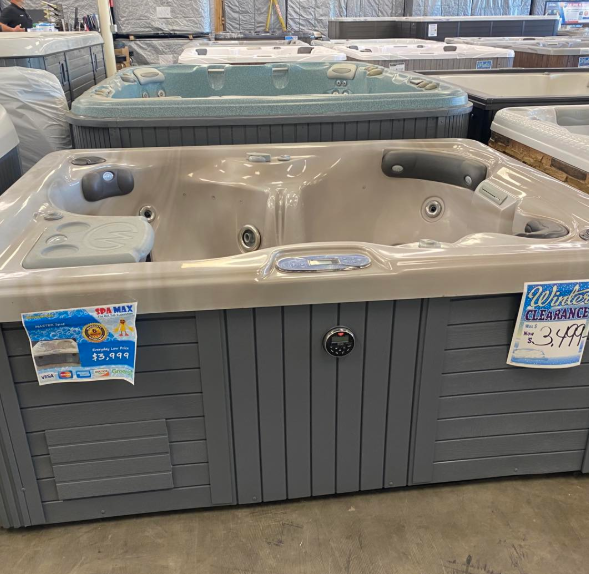 A tan and grey hot tub on display in a store, featuring a clearance sign and price tag.