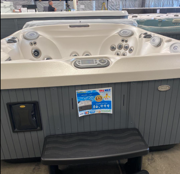 A gray and white hot tub with a black step stool in front, featuring a price tag of $6,499 on the front panel.