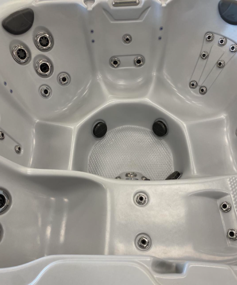 An empty, light grey hot tub interior with multiple built-in seats and various circular massage jets.