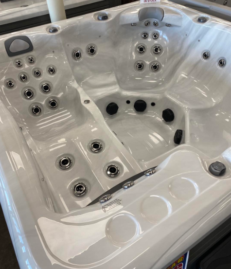 A white, multi-seat hot tub with built-in jet nozzles and cup holders, displayed indoors.