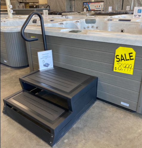 A black two-step hot tub staircase with a safety handrail positioned in front of a gray hot tub with a sale price tag.