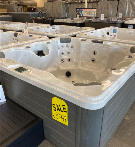 A light-colored hot tub with a yellow sale tag reading $2,999 in a showroom filled with other hot tubs.