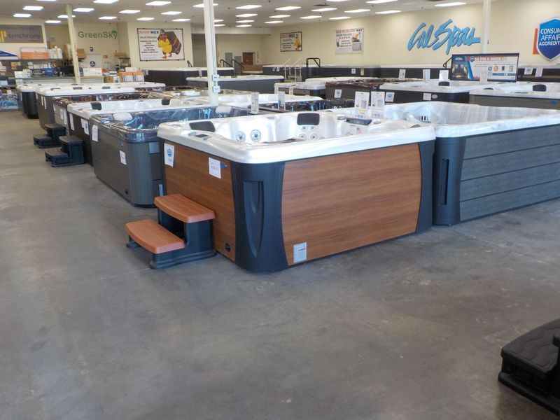 A showroom floor filled with various models of hot tubs and spas, featuring wooden and dark-colored exterior panels.