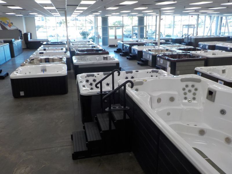 A showroom floor displaying multiple white and dark-colored hot tubs and spas with stair access for viewing.
