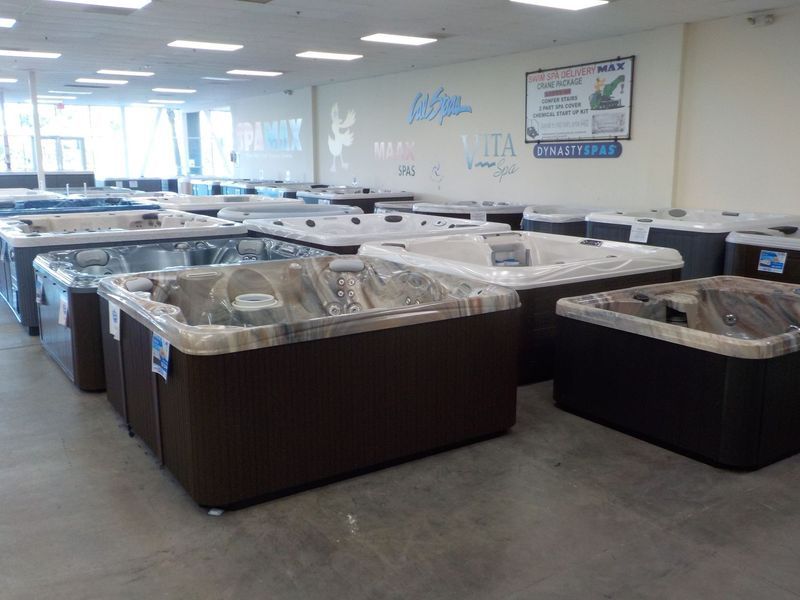 A showroom filled with various models of brown and grey hot tubs arranged in rows under indoor lighting.