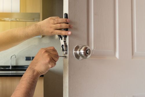 Hands using a screwdriver to install a silver door lock on a beige interior door.