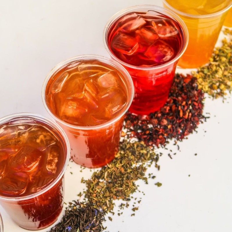 Three cups of iced tea are next to a pile of tea leaves.