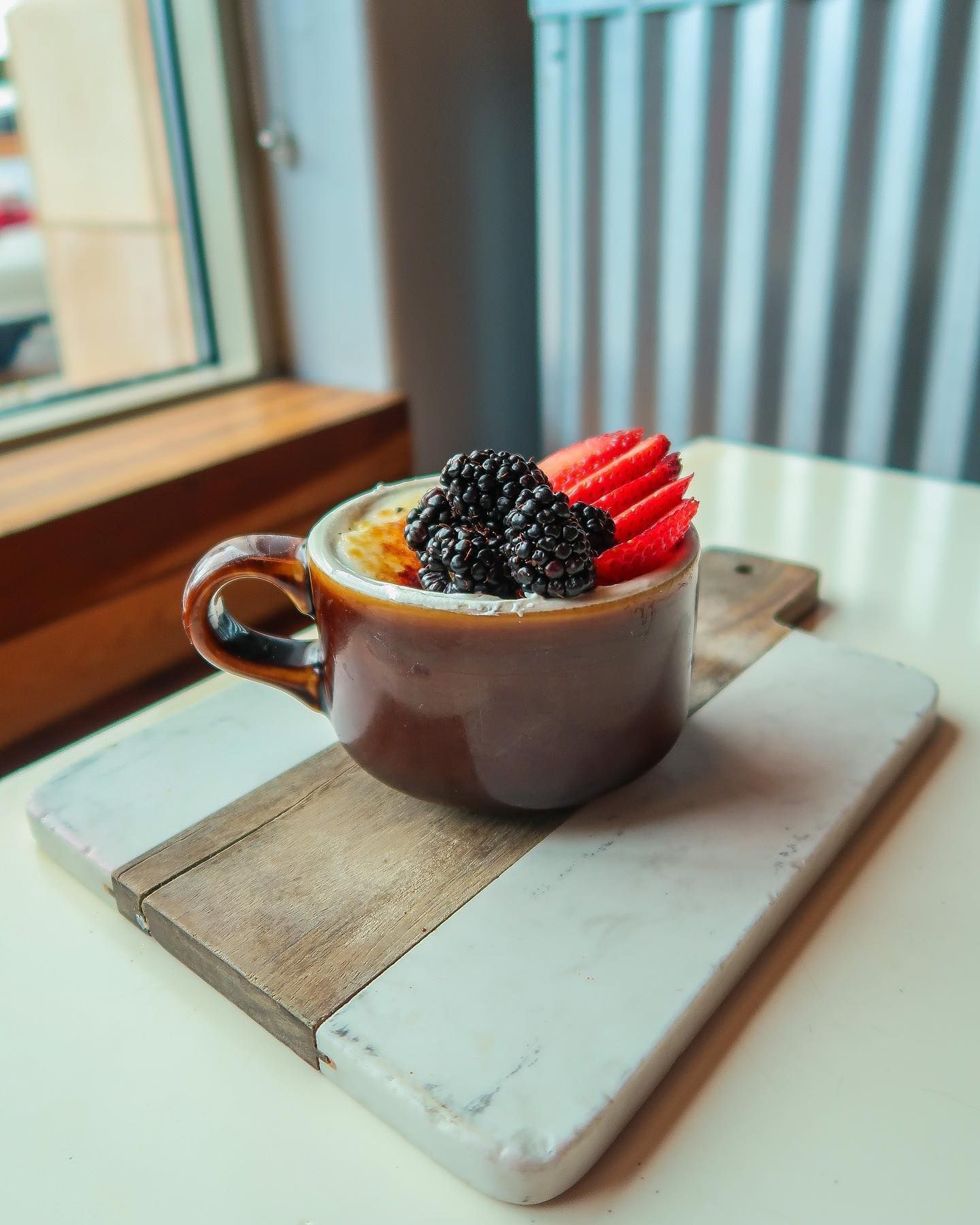 A cup of food with berries and strawberries on a cutting board on a table.