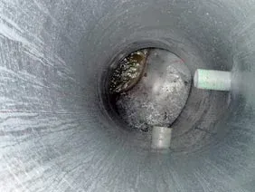 Inside a metal pipe, a ball-shaped object with debris, plus two white tubes extending from the side.