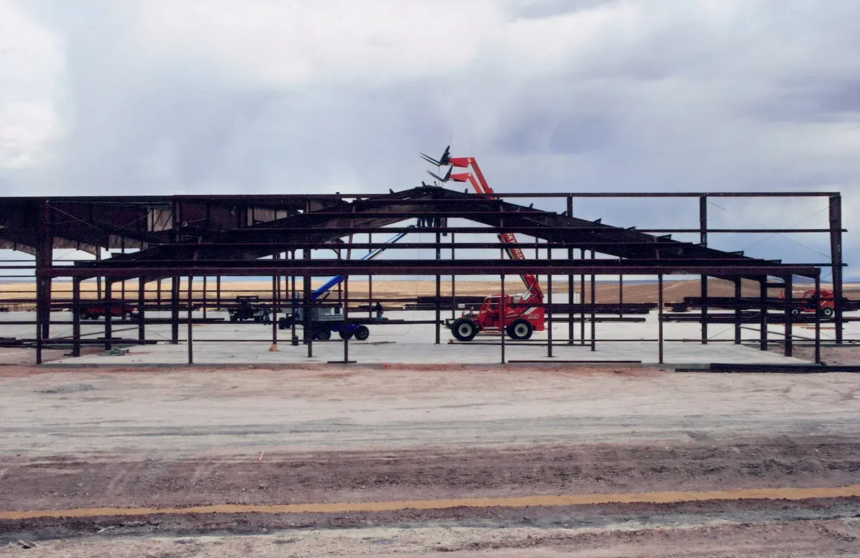 Steel framework of a building under construction, with a red lift reaching towards the roof on a cloudy day.