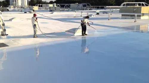 Two workers spraying white coating on a large, flat roof.