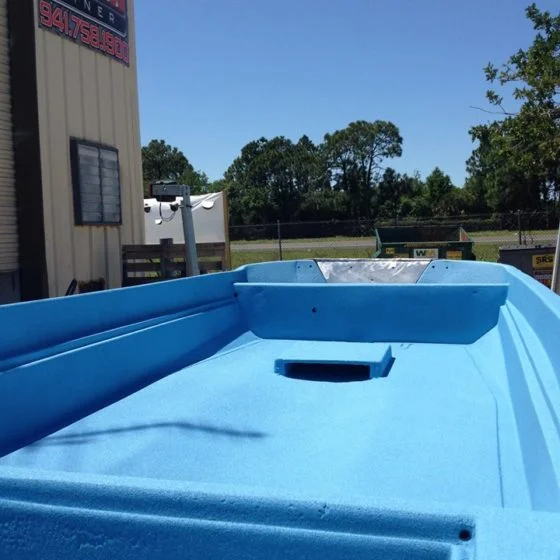 Blue boat interior with open hatch, trees, and a building in the background under a blue sky.