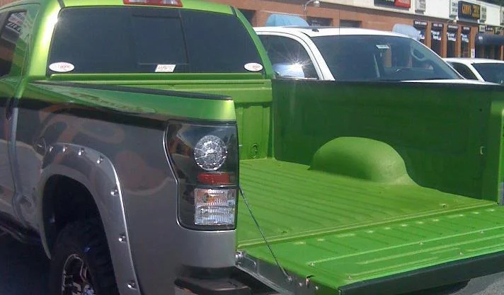 Green and gray truck bed, tailgate open, parked outdoors.