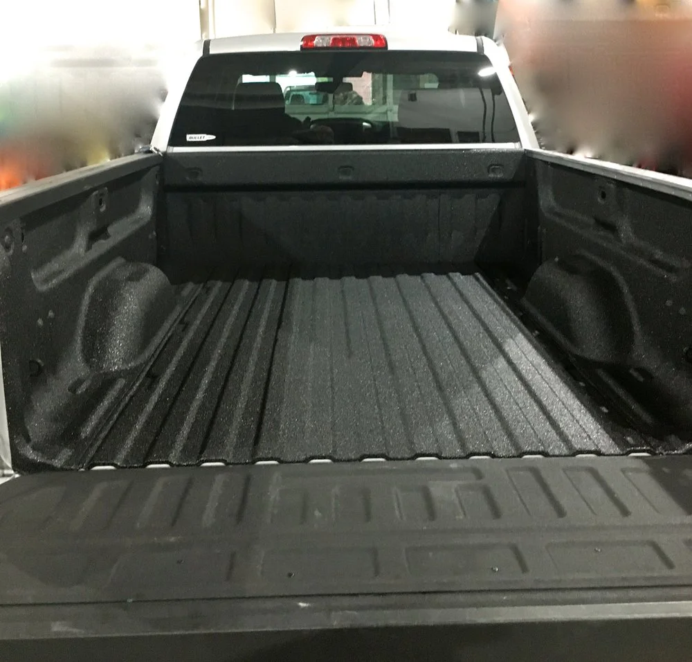 Empty truck bed with black bed liner. Rear view, indoors, looking into the bed.