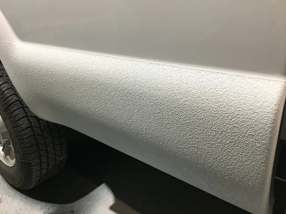 White truck bed with textured coating near a tire.