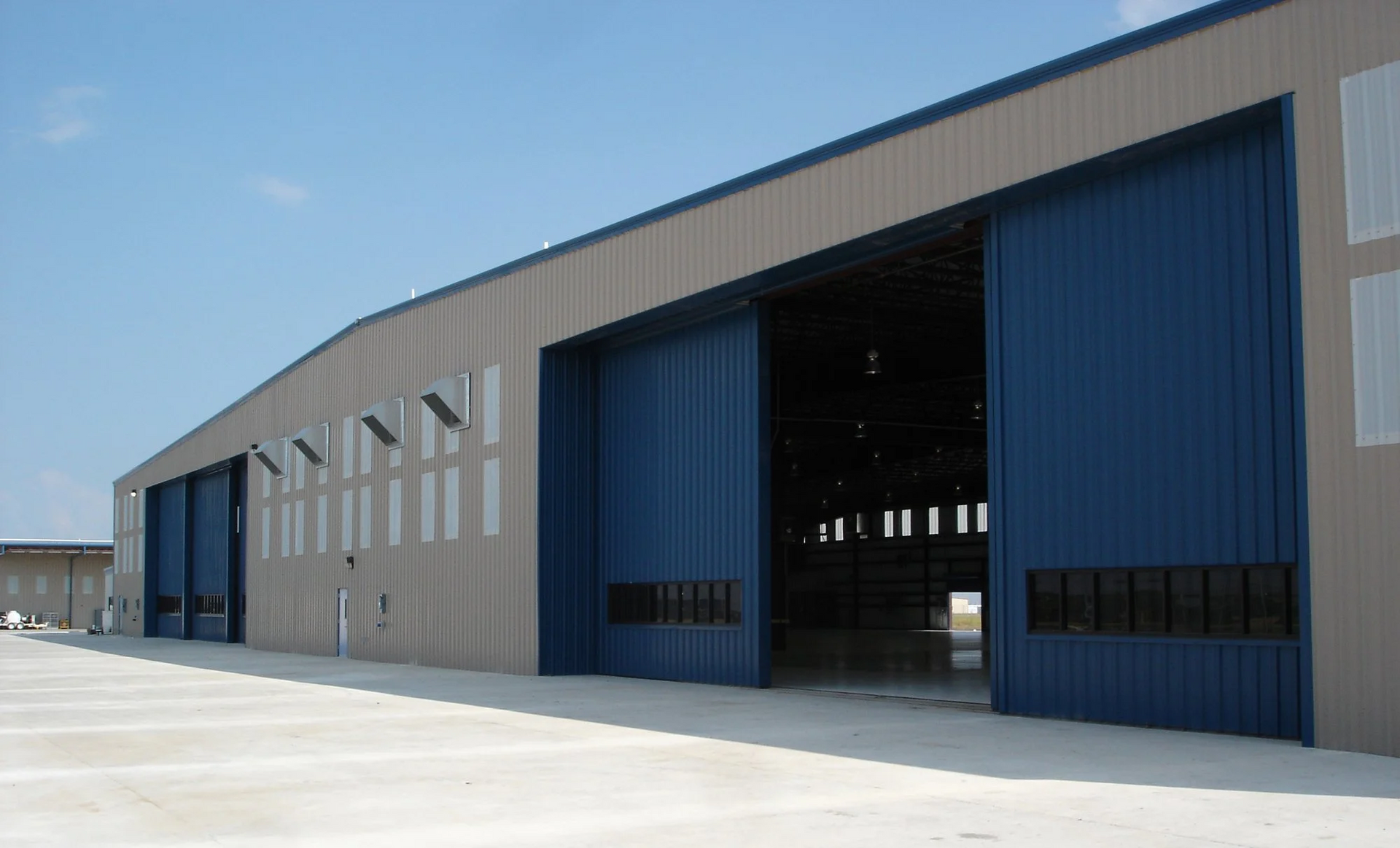 Large metal hangar with blue sliding doors open, set against a clear blue sky.