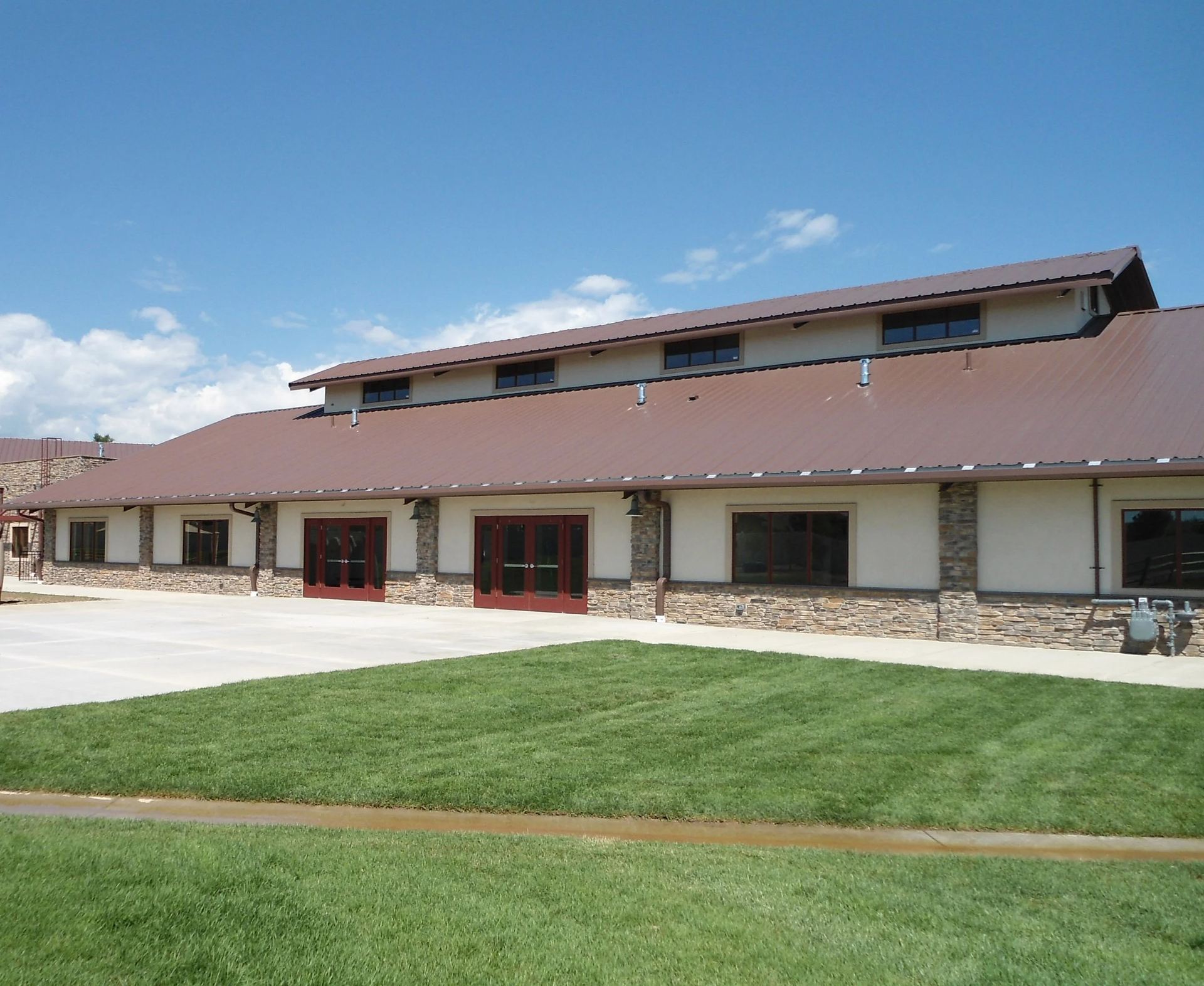 Building with brown roof, stone accents, and large windows, in front of green lawn, under a blue sky.