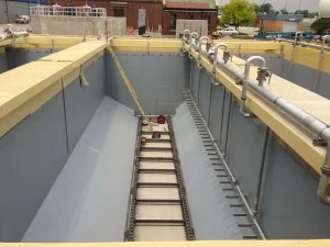 Industrial wastewater treatment tank. Gray interior, yellow trim. Ladder and conveyor system present.