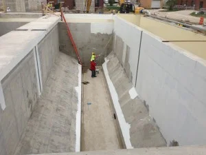 Construction workers in a concrete tank, applying sealant. Light concrete with some white and red accents.