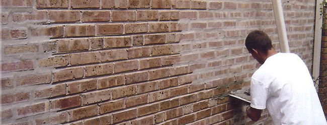 A person plastering a brick wall, adding mortar to the bricks.