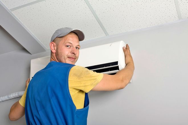 Technician installing a white wall-mounted air conditioner on a ceiling-high wall