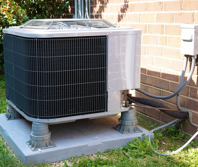 Outdoor air conditioner unit beside a brick wall on a concrete pad with connected hoses