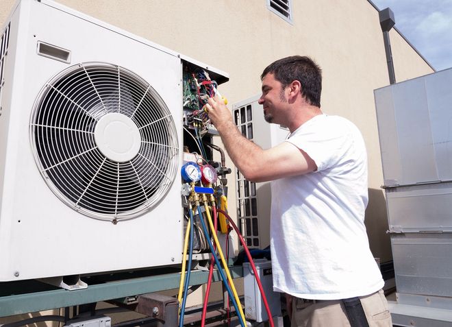 Technician repairing rooftop HVAC unit with tools and gauges