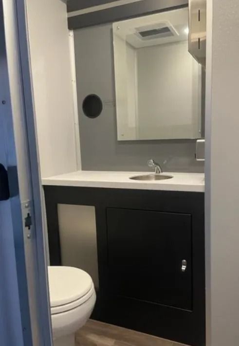 Accessible restroom with toilet, sink, mirror, and black vanity cabinet