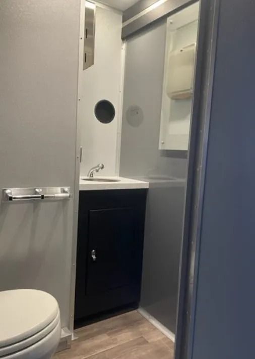 Small bathroom with toilet, sink cabinet, mirror, and gray walls visible through an open door.