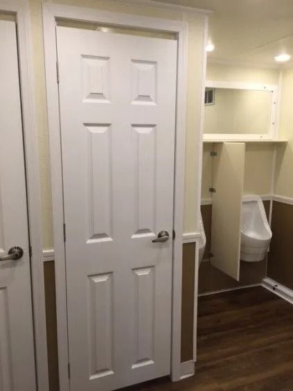Bathroom hallway with a white paneled door and visible toilet stall in the background.