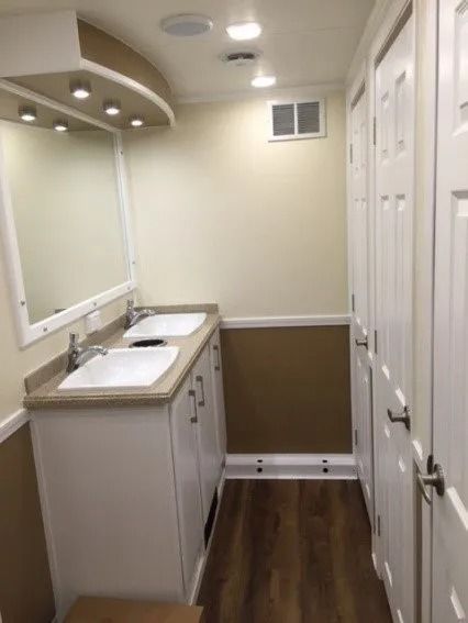 Narrow bathroom with double sinks, white cabinets, mirrors, and wood-look flooring