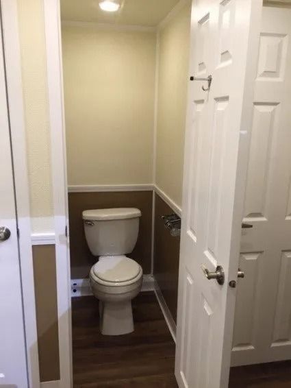 Small beige bathroom with a toilet, wood-look floor, and open white door.