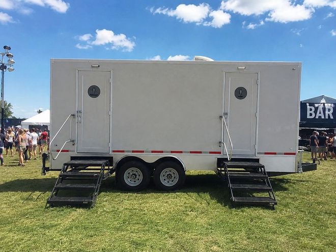 Portable restroom trailer with stairs, set outdoors in a parking lot