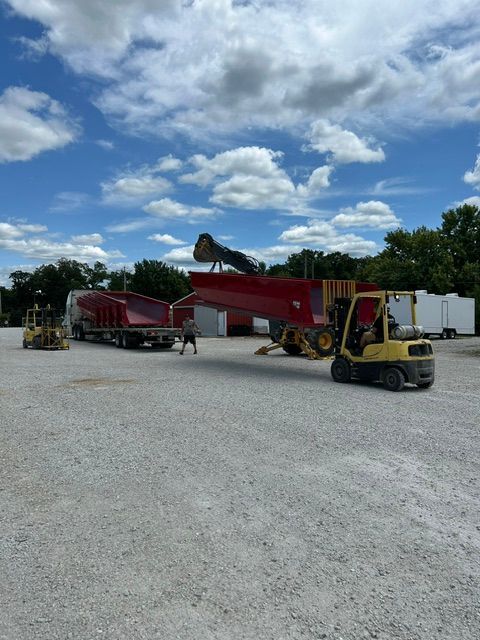 Red truck on gravel lot with forklift and trucks under a cloudy sky