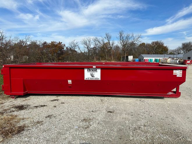 Red metal dumpster in a gravel lot under a blue sky