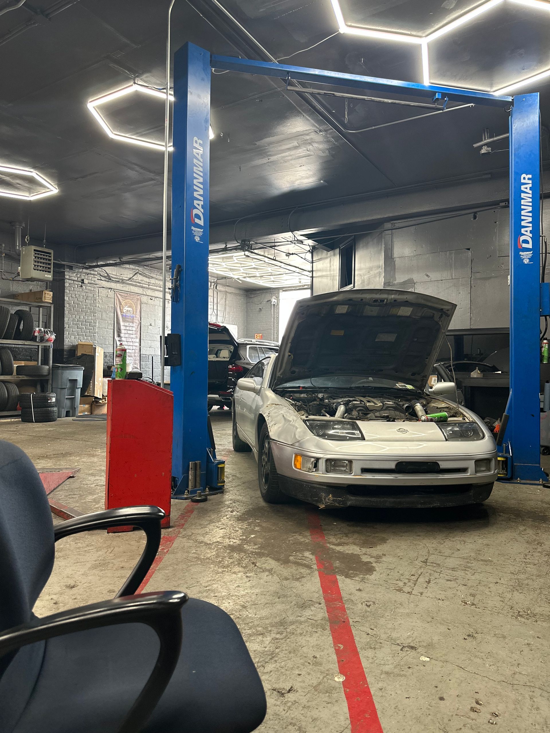 A white car with the hood up is on a lift in a garage.