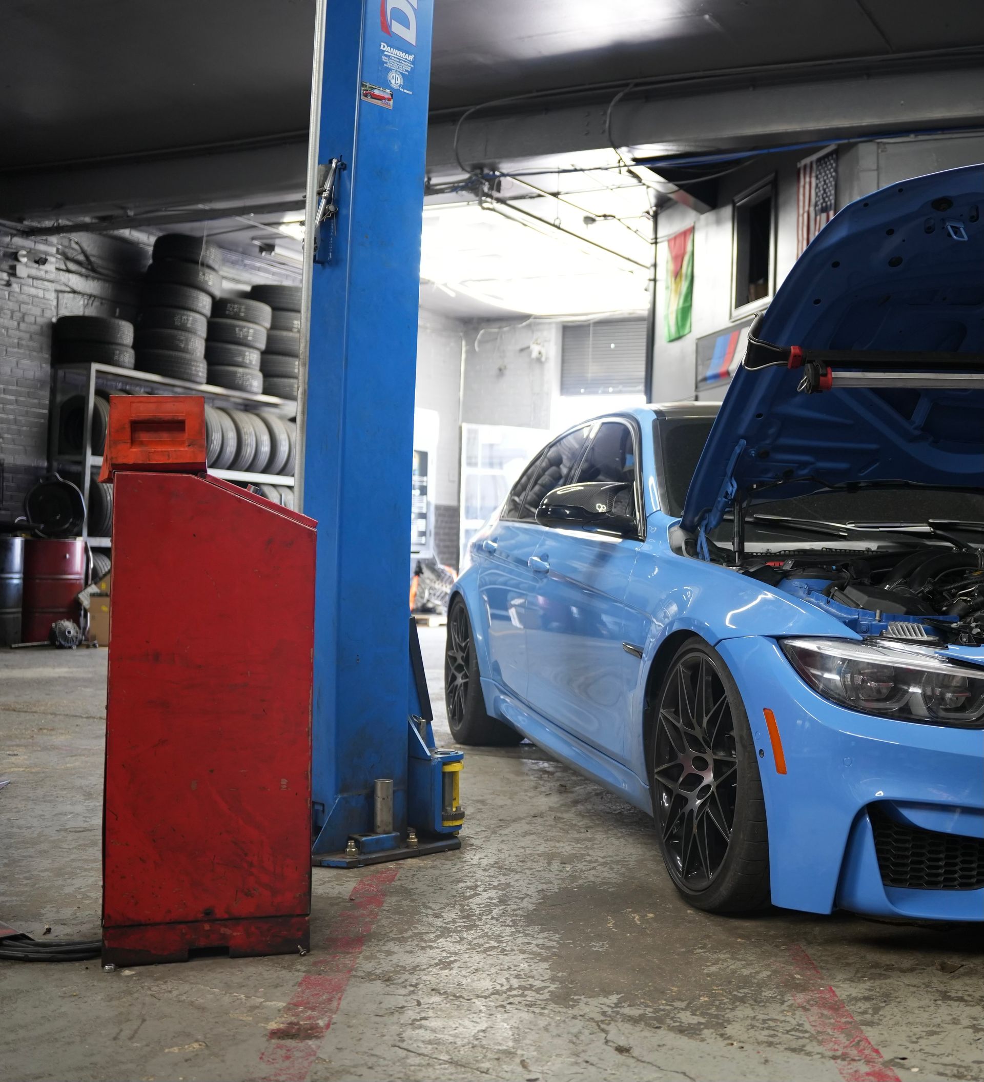 A blue car with the hood up is on a lift in a garage.