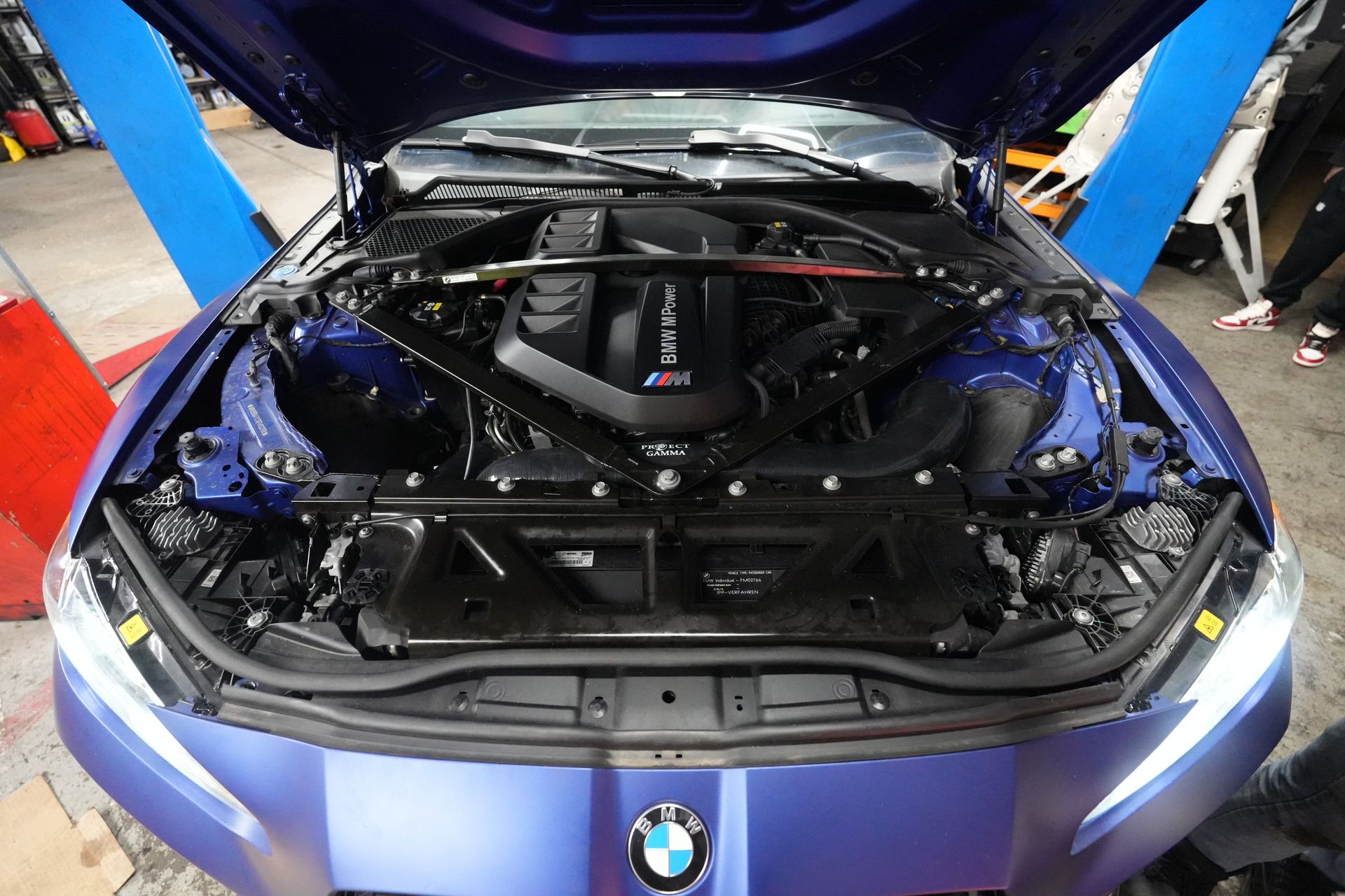 The engine of a blue bmw is shown with the hood open.