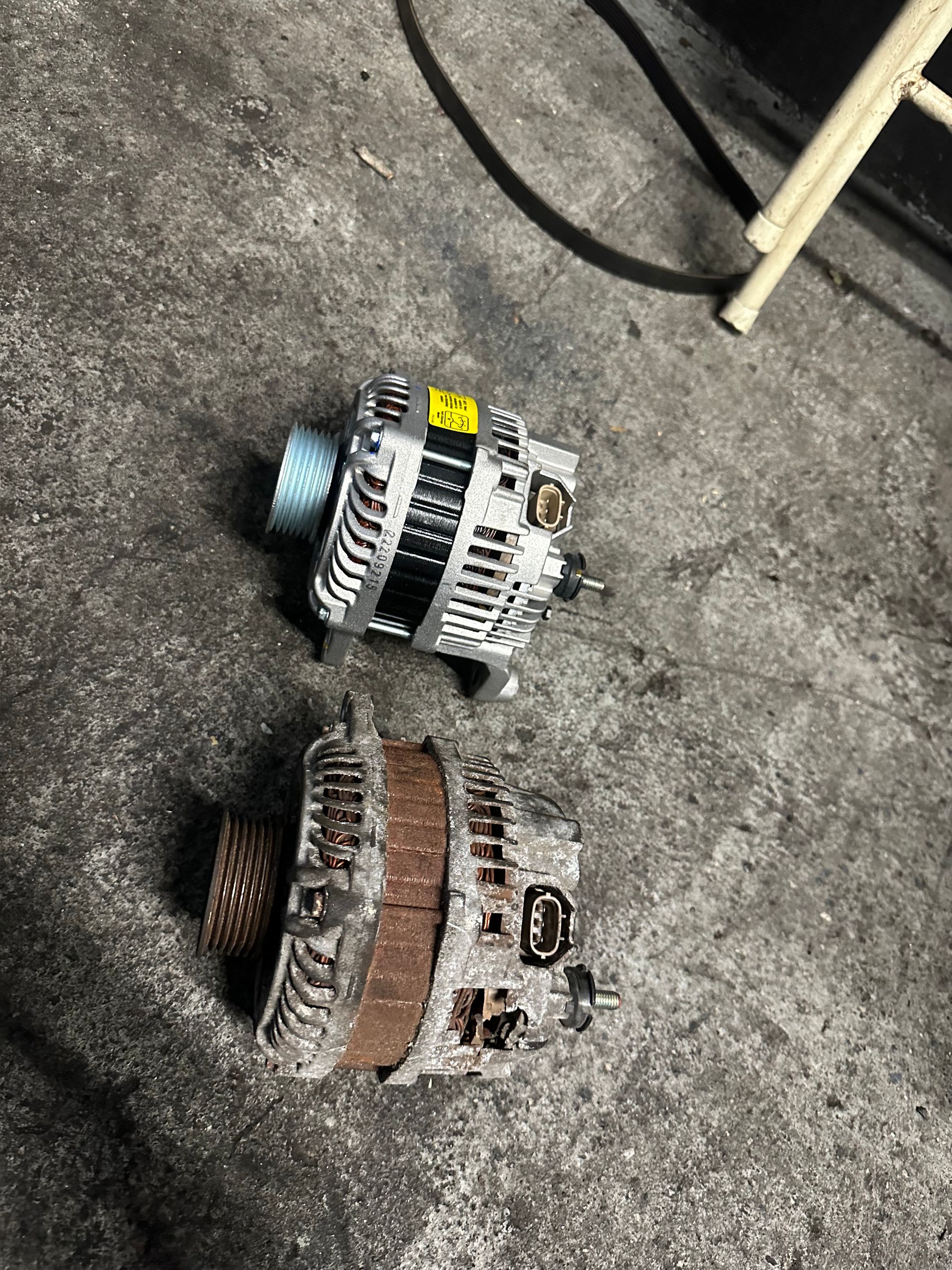 Two alternators are sitting on the ground next to each other.