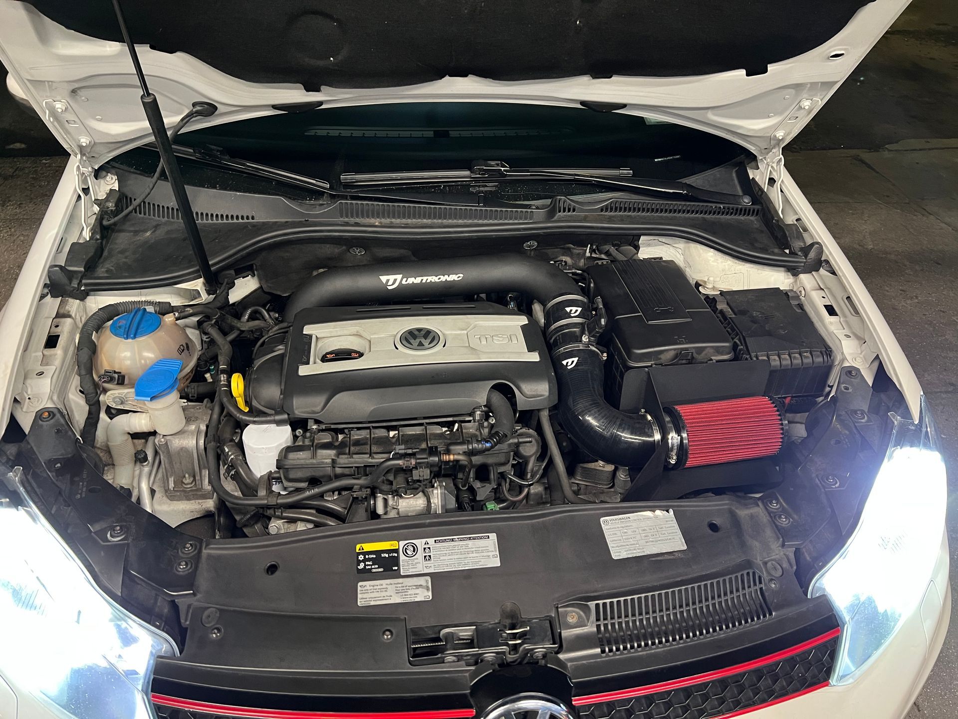 The engine of a white car is shown with the hood open.