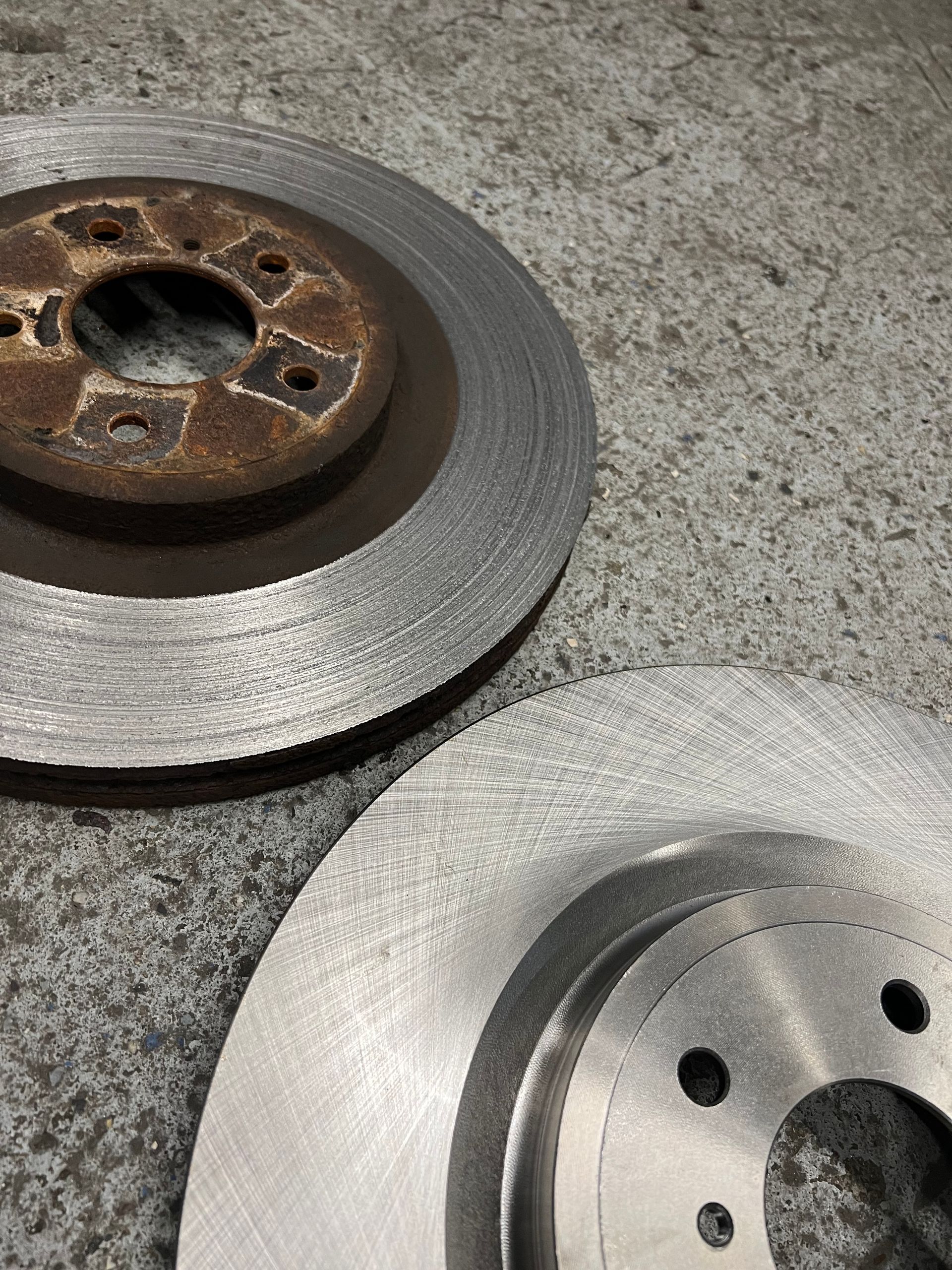 A close up of two brake rotors on a concrete surface.