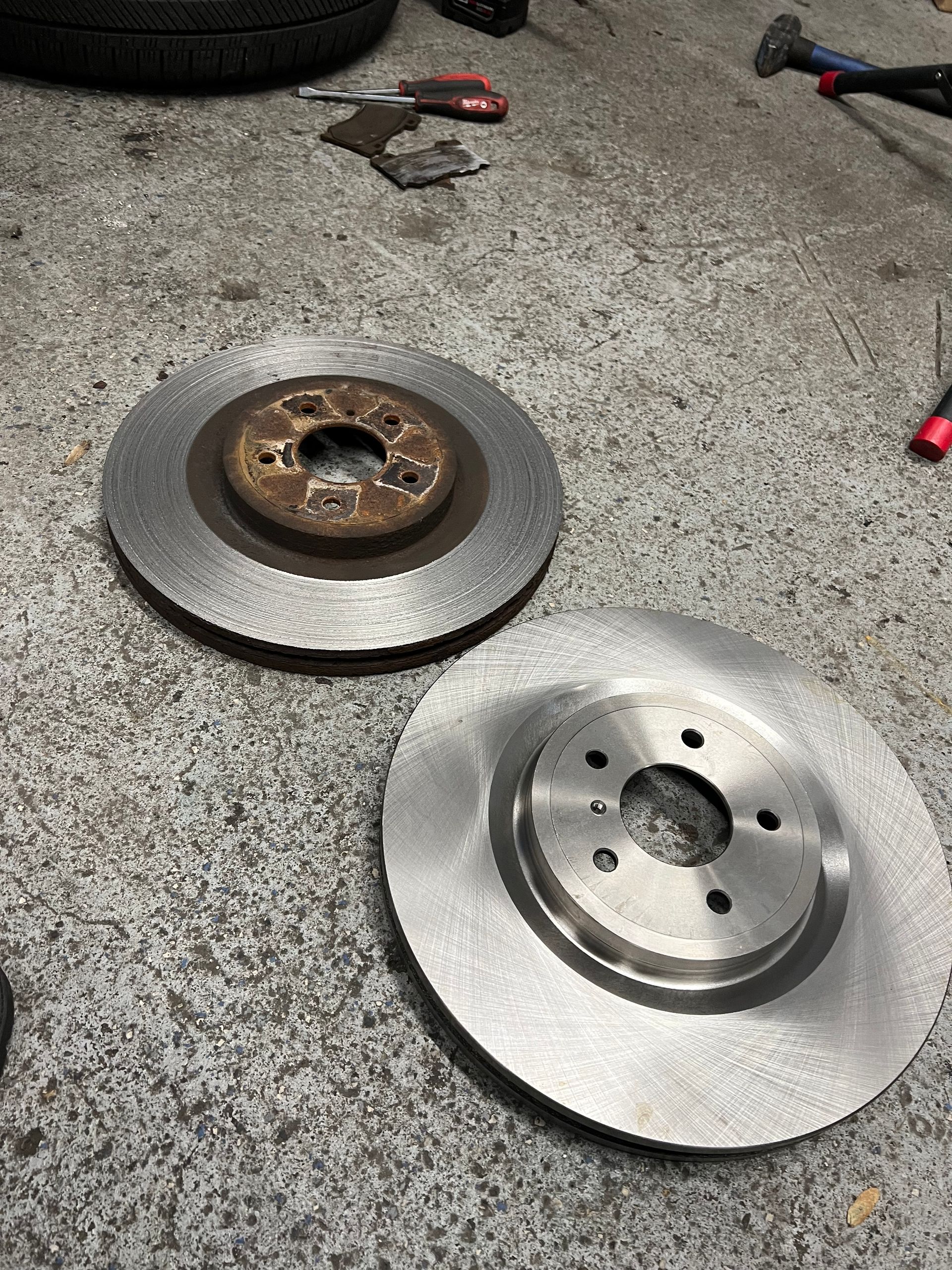 Two brake rotors are sitting on the ground next to each other.