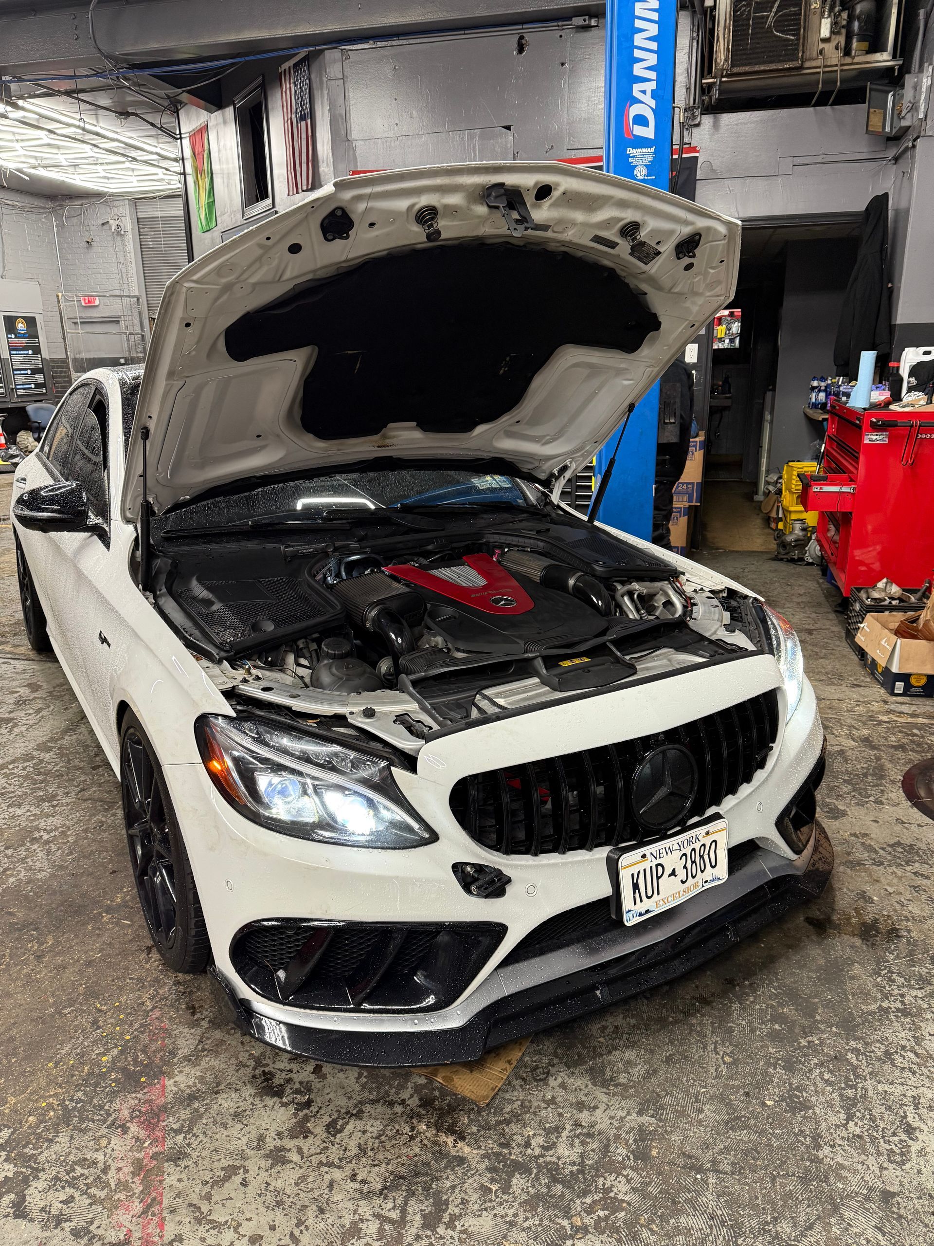 A white mercedes benz with the hood up in a garage.