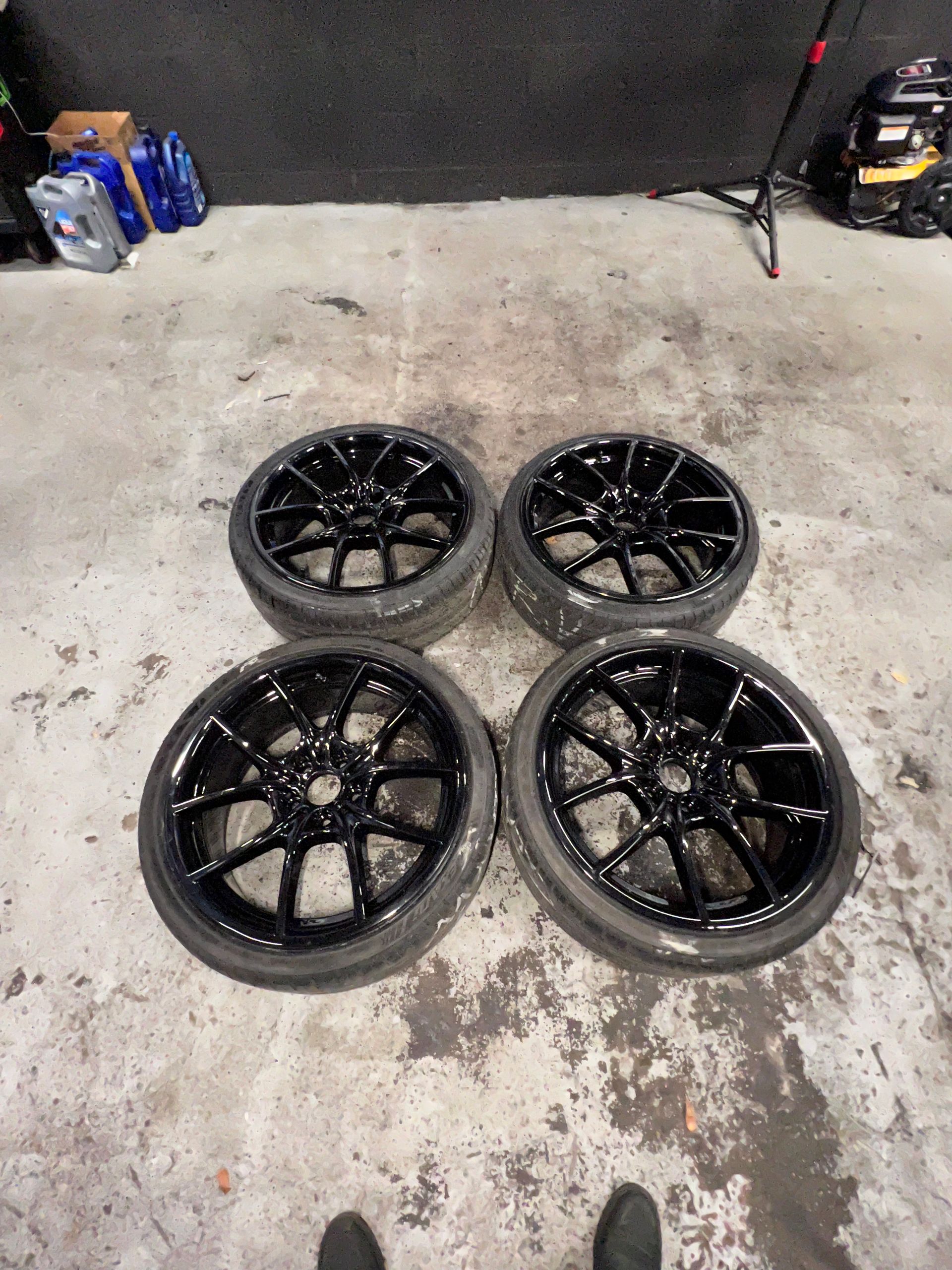 A person is standing next to a set of black wheels and tires.