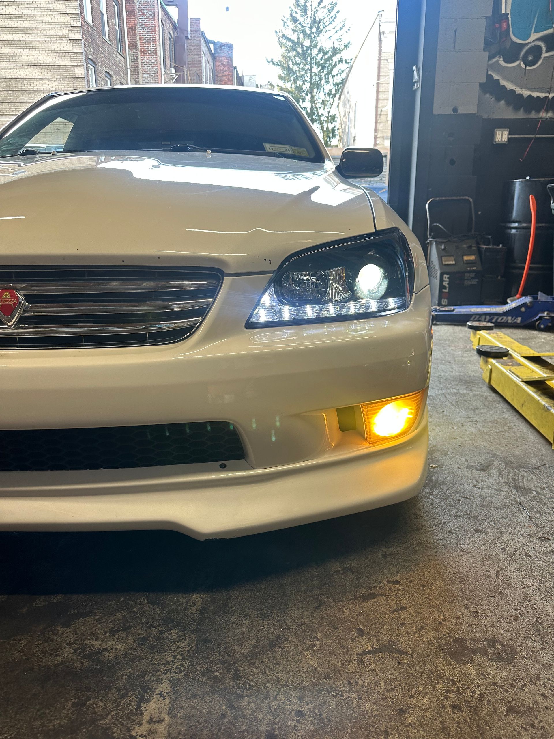 A white car with a yellow headlight is parked in a garage.