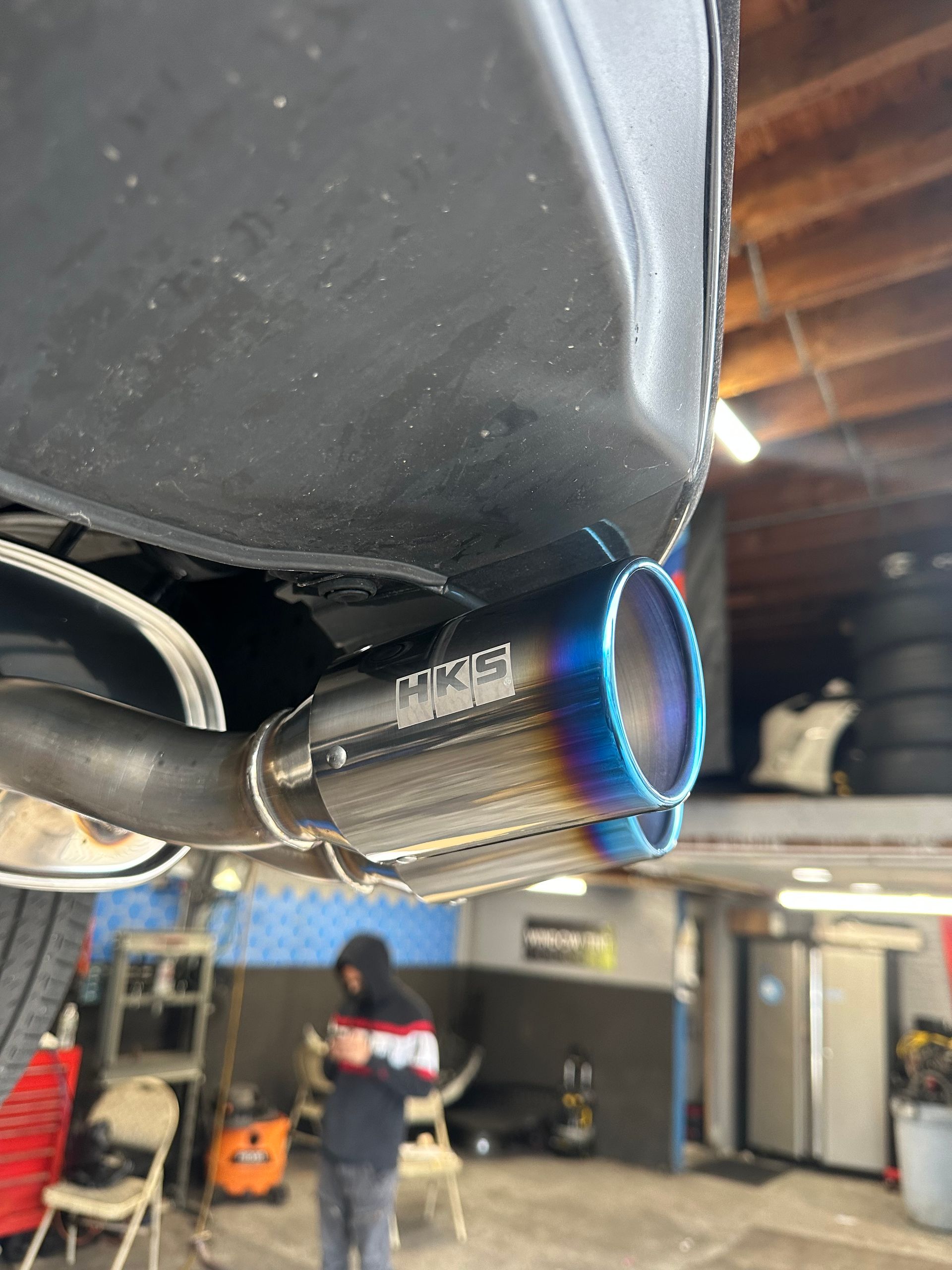 A person is standing in a garage next to a car with a exhaust pipe attached to it.