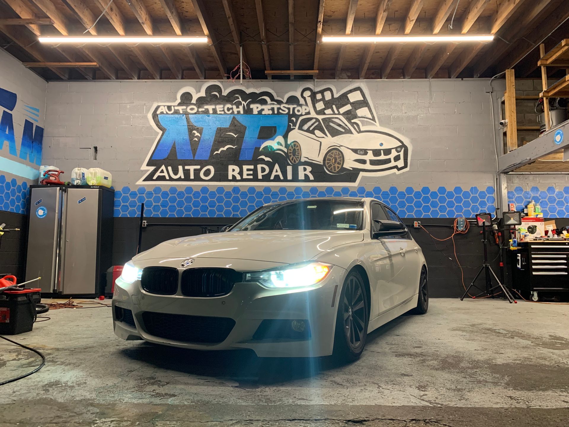A white car is parked in a garage with a sign on the wall that says auto repair