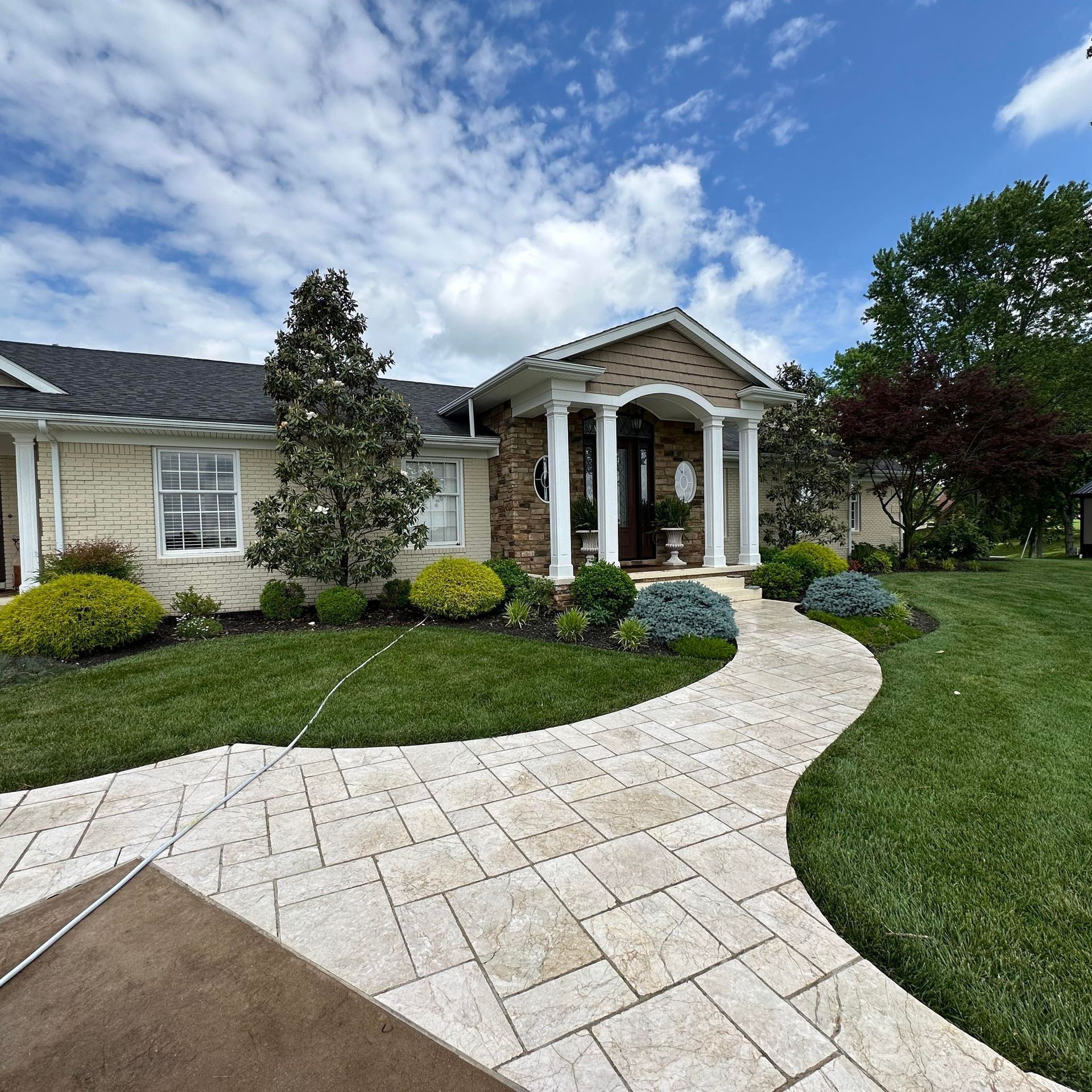 Two-story gray house with white garage doors, stone accents, and a blue sky.