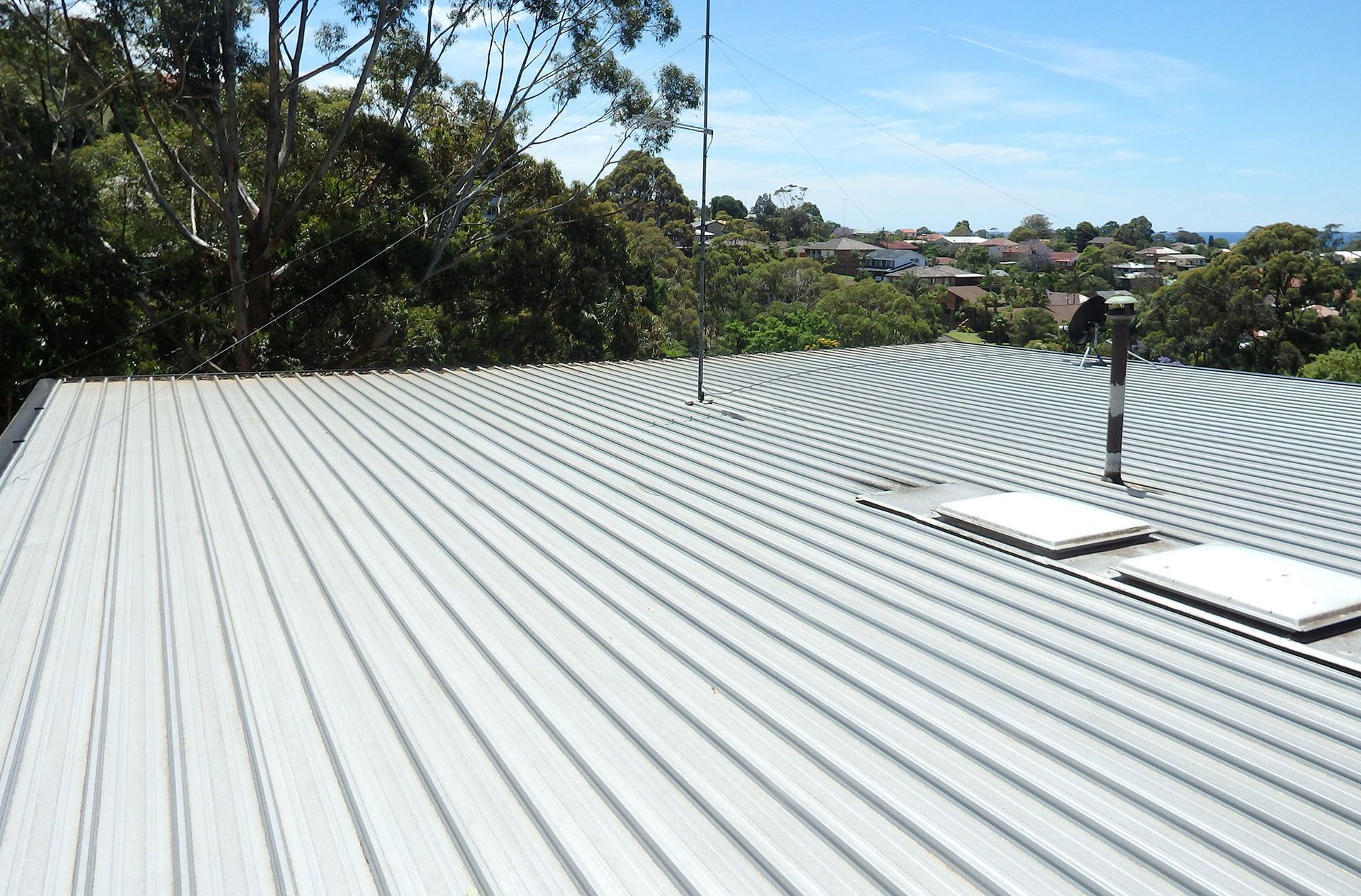 Metal roof with curved ridges, two skylights, a radio antenna, and a scenic view of trees and houses.
